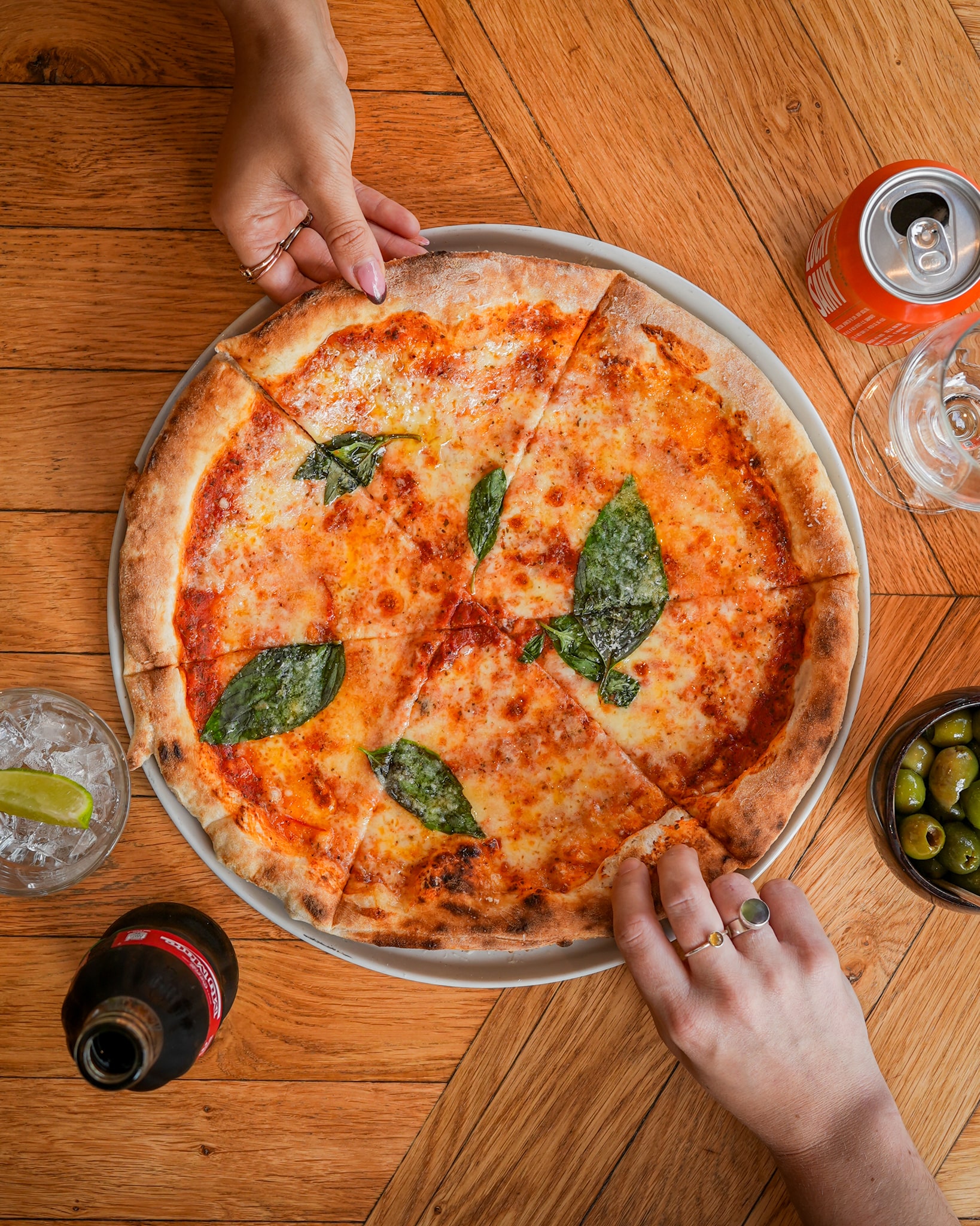 A tempting pizza on a table with two hands reaching out, representing Leaven Pizza Hereford, Herefordshire, London.